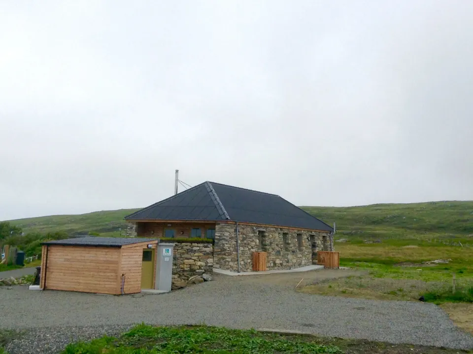 John’s Bunkhouse: a low stone building with a dark slate roof and timber bike shed, set on open moorland