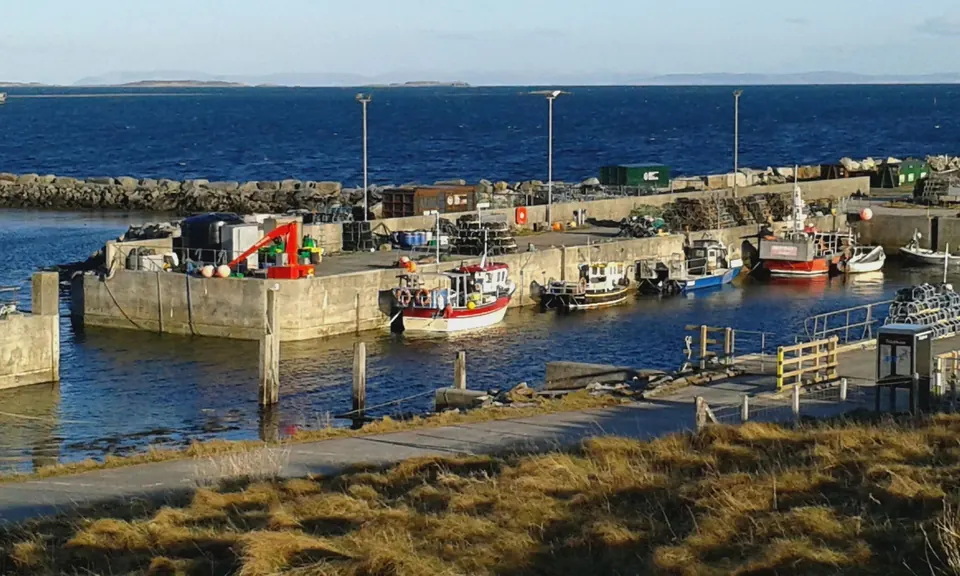 Fishing boats moored in the stone harbour at Berneray on a calm, bright day